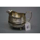 An early 19th century silver milk jug with angular handle, ribbed bands, on four ball feet, marks