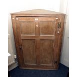 A George III pine wall mounting corner cupboard, the moulded cornice over a four panel door with