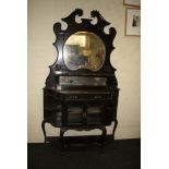 An Edwardian ebonised mirror backed vitrine, the broken scrolled pediment over trinket shelves