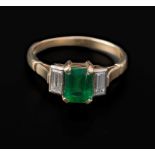 An emerald and diamond three stone half hoop ring, the step cut , cut-cornered emerald in claw mount