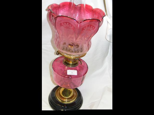 A brass oil lamp with cranberry glass etched shade