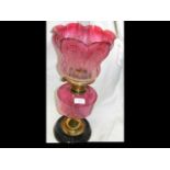 A brass oil lamp with cranberry glass etched shade