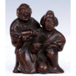 A JAPANESE HARDWOOD NETSUKE of a man pouring his wife a drink, signature to his back.