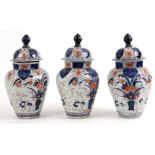 A SET OF THREE 19TH CENTURY IMARI OCTAGONAL FACETED TAPERING GINGER JARS AND COVERS decorated with