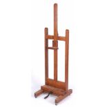 AN EARLY 20TH CENTURY OAK ADJUSTABLE EASEL with rack and pinion adjustment, under casters and