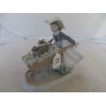 A Lladro figure of girl pushing puppies in a wheel barrow.