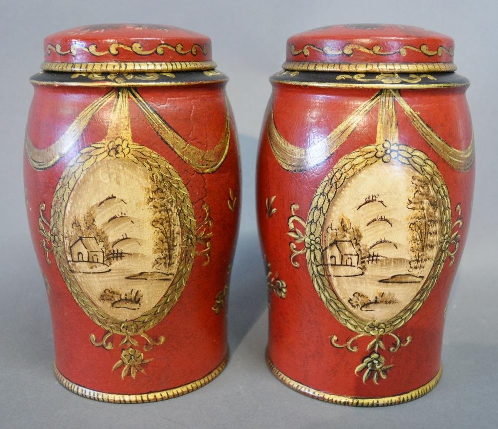 A Pair of Tole Ware Small Covered Canisters with gilded bow and ribbon decoration upon a red and