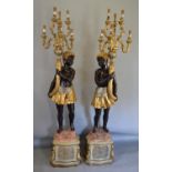 A Pair of Blackamoor Floor Standing Candelabra each with six shaped arms above figural supports, and