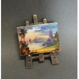 A White Metal Brooch In The Form Of An Easel With Enamel Decorated Picture