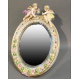 A German Porcelain Oval Table Mirror Surmounted With Cupid and foliate encrusted decoration, 36cm by