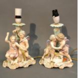 A Pair Of German Porcelain Table Lamps Each Decorated With Putti upon shaped bases, 23cm tall