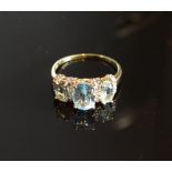 A Yellow Gold Blue Topaz And Diamond Ring set with three oval blue topaz inter-spaced with
