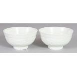 A SMALL PAIR OF MING STYLE MOULDED PORCELAIN BOWLS, applied with a pale celadon glaze, each base