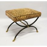 A BRONZE AND IRON CROSS FRAME STOOL with padded top. 1ft 9ins long x 1ft 4ins high.