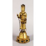 A GILT BRONZE FIGURE OF A STANDING EASTERN DEITY, on an octagonal base. 12ins high.