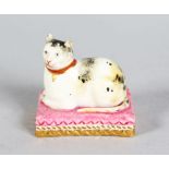 A MINIATURE DERBY CAT, lying down on a pink and gold cushion. Derby Mark in Red. 1.5ins long, 1ins