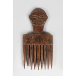 A CARVED TRIBAL COMB, the handle on a face. 8ins long.