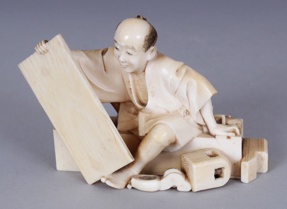 A GOOD QUALITY SIGNED JAPANESE MEIJI PERIOD IVORY OKIMONO OF SEATED CARPENTER, holding between his
