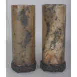A PAIR OF EARLY 20TH CENTURY CHINESE JADE CYLINDRICAL VASES, each supported on a fixed carved wood