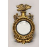 A REGENCY GILTWOOD CONVEX MIRROR, with eagle and anthemion cresting and leaf carved decoration below