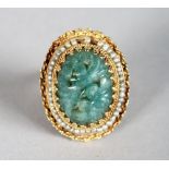 A GOLD AND JADE RING, the oval jade stone with carved decoration, surrounded by seed pearls.