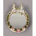 A MEISSEN STYLE PORCELAIN MIRROR, with a pair of cherubs and floral encrusted frame. 12ins high.