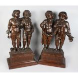 A GOOD PAIR OF CARVED WOOD STANDING CHERUBS, on rectangular base. 2ft 7ins high.