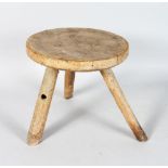 A RUSTIC WOOD CIRCULAR MILKING STOOL, 10ins diameter, on three rustic legs.