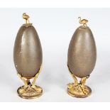 A PAIR OF ORMOLU MOUNTED EMU EGGS, the top with an emu, the base as three curving dragons. 8ins