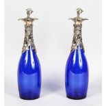 A PAIR OF BRISTOL BLUE BOTTLES, with plated cast mounts and stoppers. 13.5ins high.