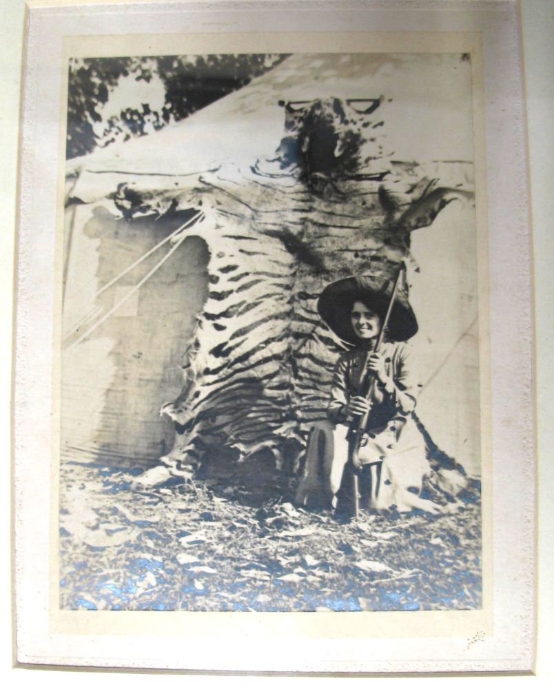 [BIG GAME] framed photograph of armed woman hunter in the field, tiger-skin in background, f &g, ca.