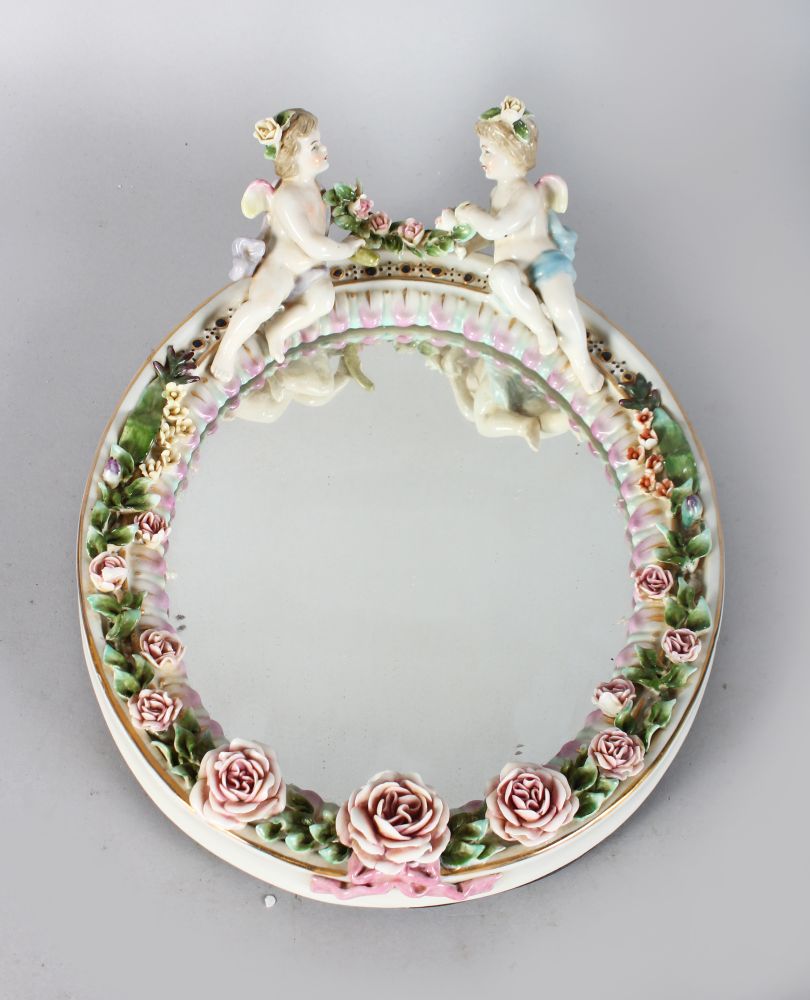 A SMALL MEISSEN DESIGN OVAL ENCRUSTED MIRROR with two cupids. 12ins long.