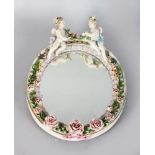 A SMALL MEISSEN DESIGN OVAL ENCRUSTED MIRROR with two cupids. 12ins long.