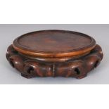 A SIMILAR LARGER CHINESE CIRCULAR WOOD VASE STAND, supported on ruyi-form feet, 8.25in wide at