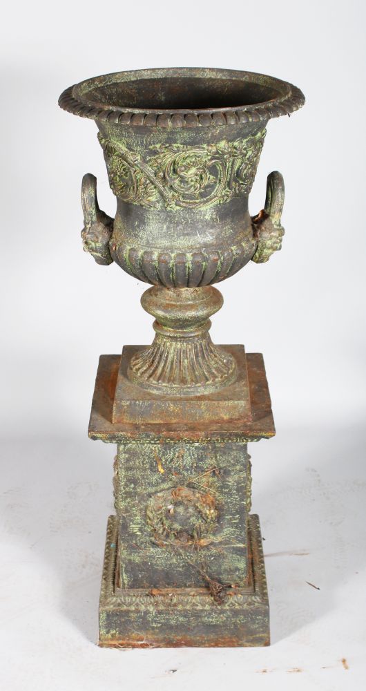 A VICTORIAN CAST IRON URN SHAPED TWO-HANDLED VASE ON STAND with mask handles. 3ft 8ins high