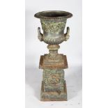 A VICTORIAN CAST IRON URN SHAPED TWO-HANDLED VASE ON STAND with mask handles. 3ft 8ins high