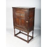 AN 18TH CENTURY OAK CUPBOARD ON STAND, the panel door enclosing a single shelf on a turned base with