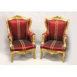 A PAIR OF CARVED GILTWOOD WINGED ARMCHAIRS, in Burgundy upholstery. Each 3ft 10ins high.