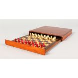 A SQUARE WOODEN TRAVELLING CHESS SET. 8ins.