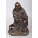 A SMALL CHINESE BRONZE FIGURE, an elderly man seated, holding a vessel in his hand. 9ins high.