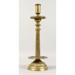 A HEAVY BRONZE CANDLESTICK, with engraved decoration, on a circular base. 15ins high.