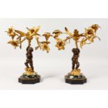 A SMALL PAIR OF FRENCH BRONZE, ORMOLU AND MARBLE CANDLESTICKS, as a cupid holding aloft two candle