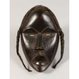 A CARVED WOOD TRIBAL MASK, with braided hair. 9ins high.