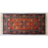 A CHINESE RUG, with terracotta ground and coloured motifs. 5ft x 2ft 4ins.