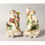 A GOOD PAIR OF CHELSEA DERBY STYLE CUPID CANDLESTICK FIGURES, modelled as putti, holding a sheath of