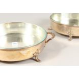 A PAIR OF CIRCULAR DISHES WITH HANDLES, with glass liners. 13.5ins wide.