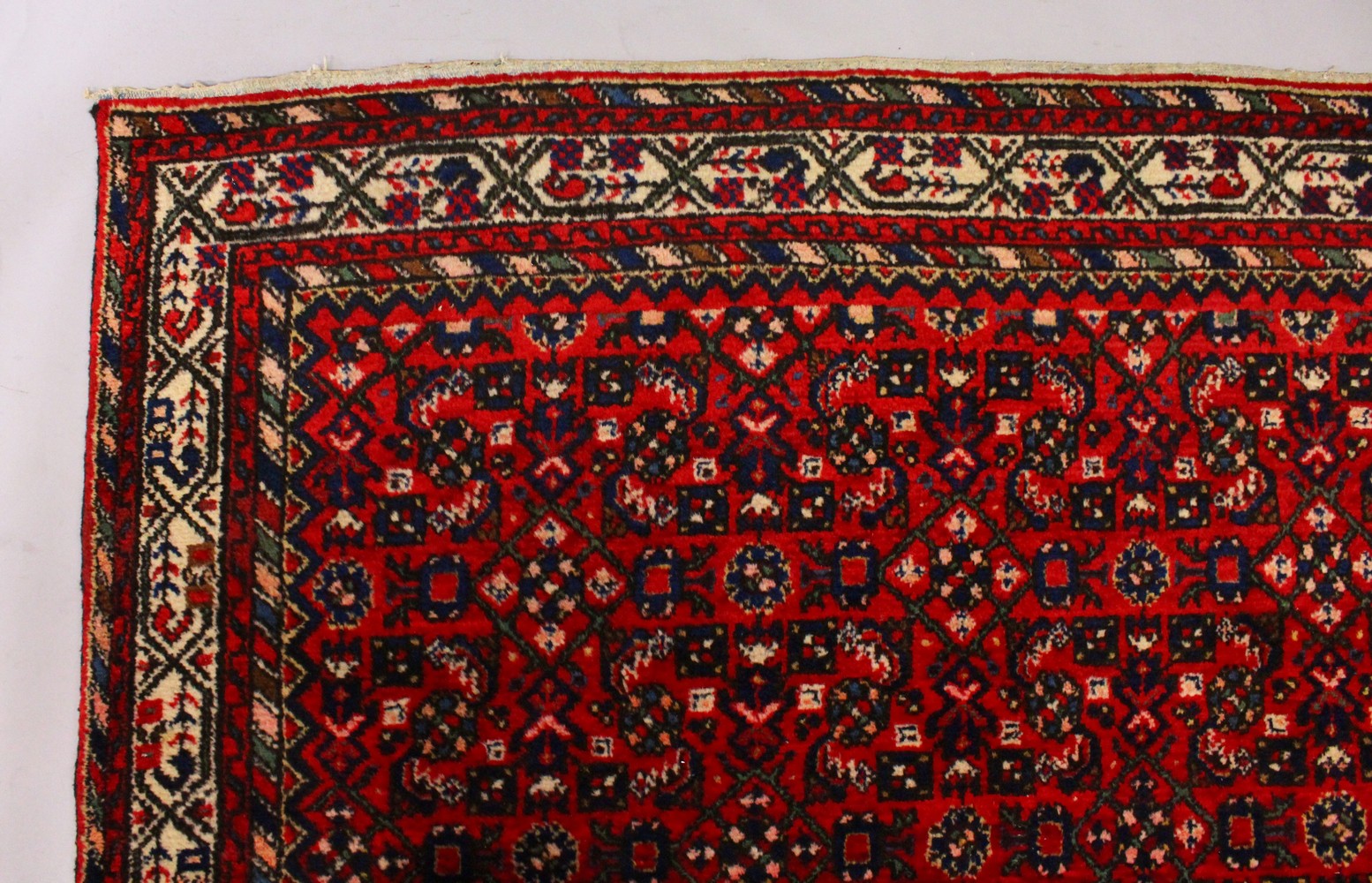 A PERSIAN CARPET, with an all-over design of motifs on a red ground. 9ft 9ins x 7ft.