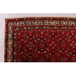 A PERSIAN CARPET, with an all-over design of motifs on a red ground. 9ft 9ins x 7ft.