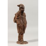 A TERRACOTTA SCULPTURE, modelled as a man wearing a coat, hands in his pockets, signed. 11ins high.