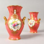 A PAIR OF ROYAL CROWN DERBY PINK TWO-HANDLED VASES, painted with a panel of flowers. 6ins high.